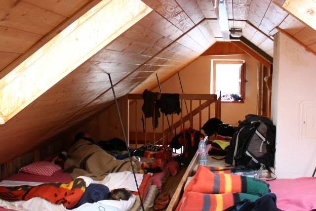 A hut dormitory under the roof: a shared mattress platform, folded blankets and everyone's kit.